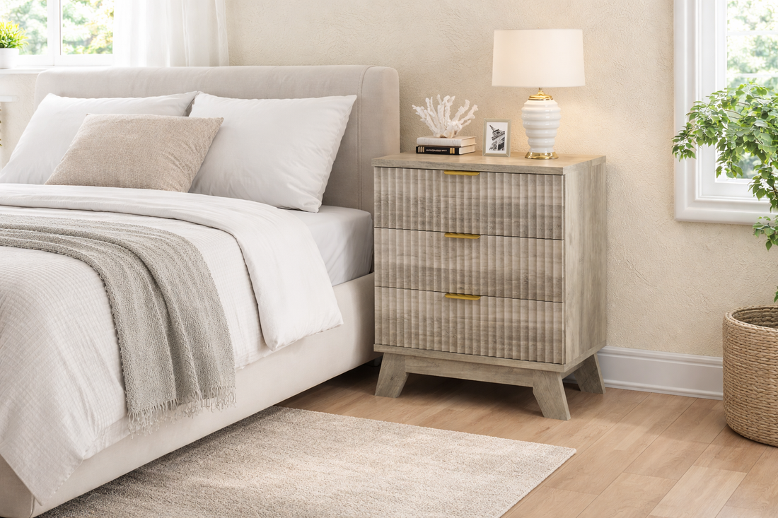 Fluted 24-inch grey wood nightstand with three drawers placed beside a beige upholstered bed in a bright small bedroom setting.