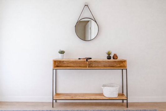 Narrow wooden console table with lower shelf placed in a small apartment entryway beneath a round wall mirror