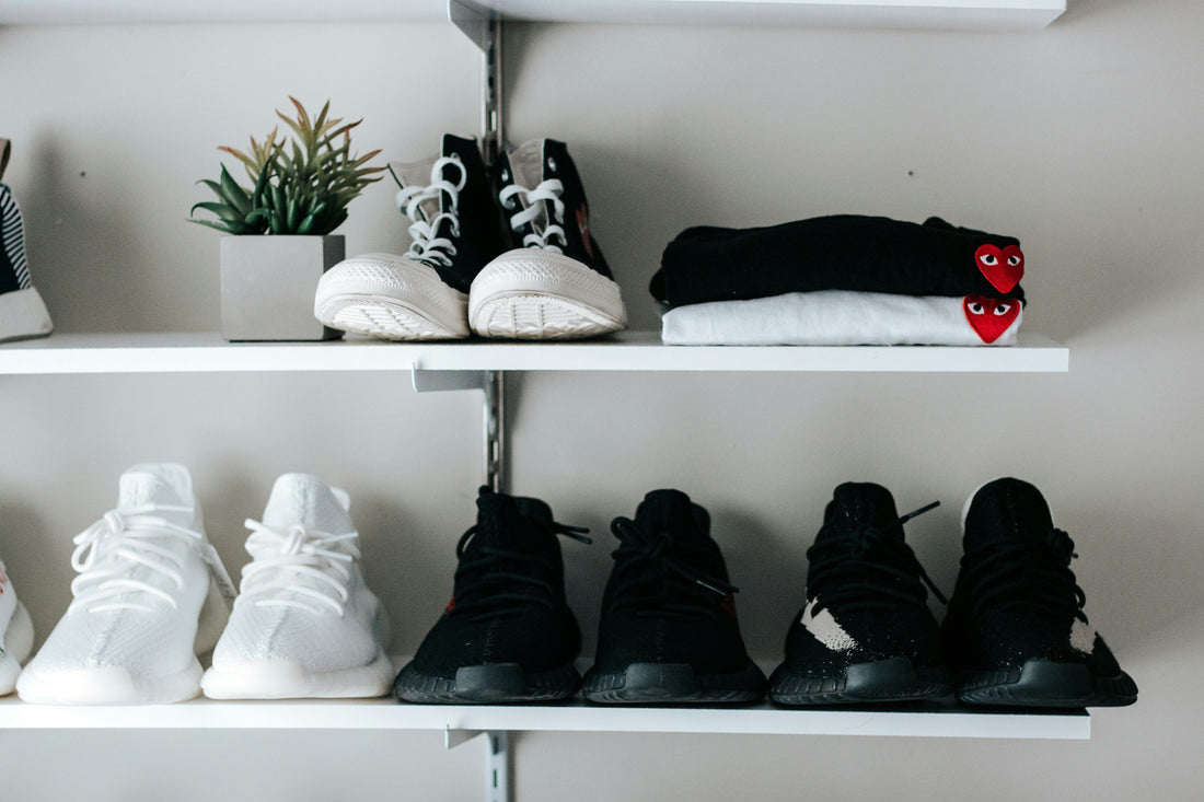 Organized shoe storage shelves in a small apartment entryway showing neatly arranged sneakers and folded clothing on minimalist white shelves.
