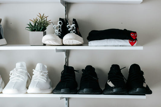 Organized shoe storage shelves in a small apartment entryway showing neatly arranged sneakers and folded clothing on minimalist white shelves.